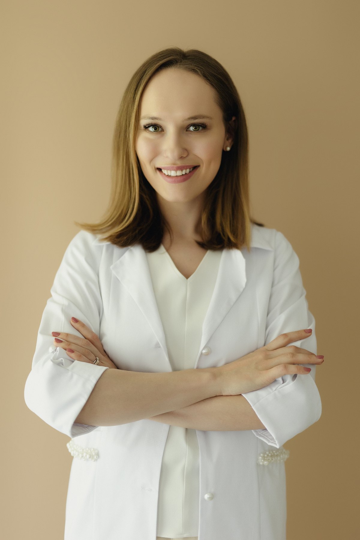 Dr. Georgiana Gheba, medic specialist dermatolog, în halat alb pe fundal bej cald